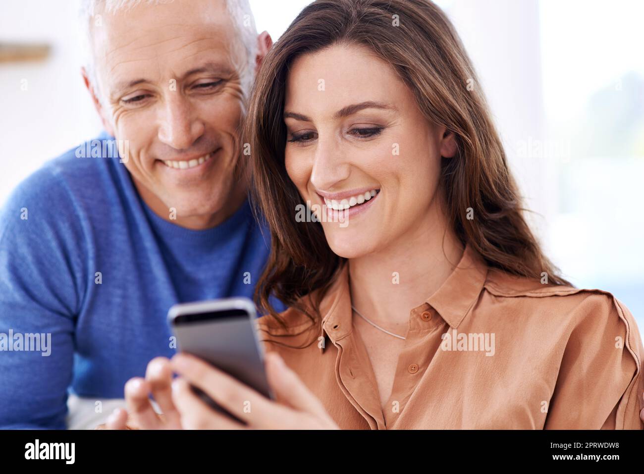 Checking out happy holiday snaps together. a happy mixed age couple smiling at messages on a cellphone. Stock Photo