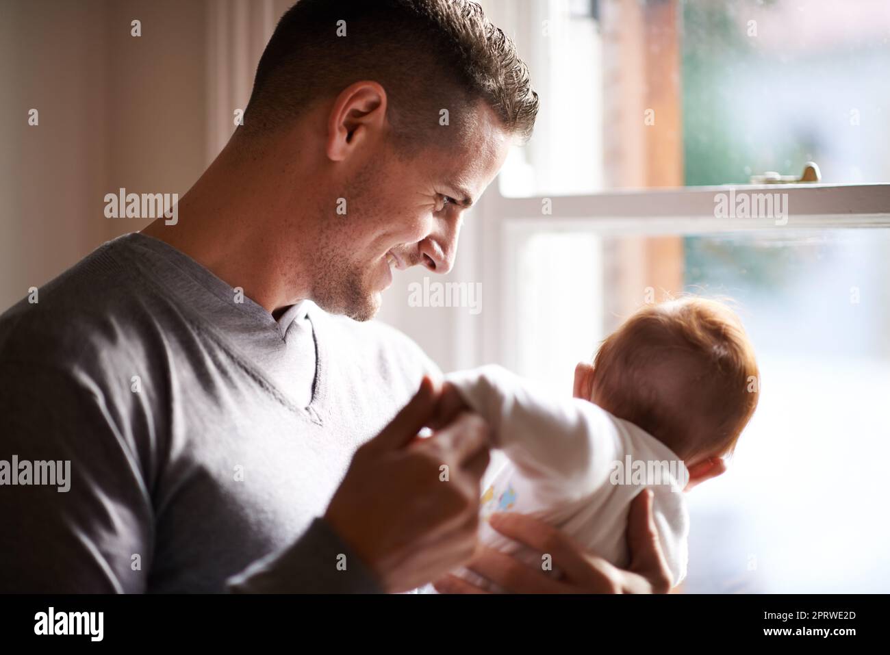 Its a big world out there but youll always be safe with me. a young father standing by a window holding his adorable baby girl. Stock Photo