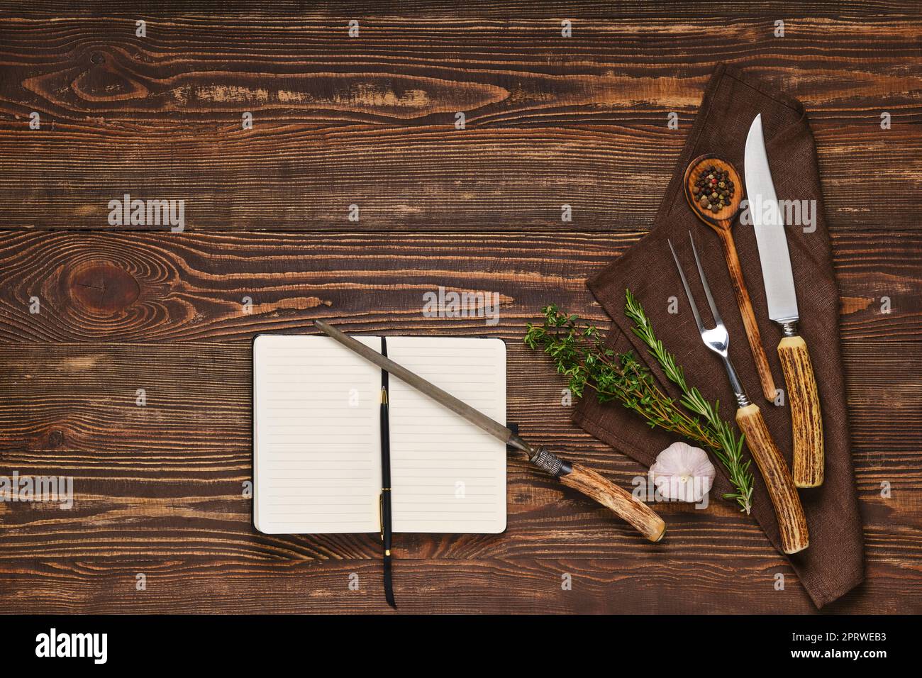 Steak fork, knife and sharpener on wooden table next to notebook Stock Photo