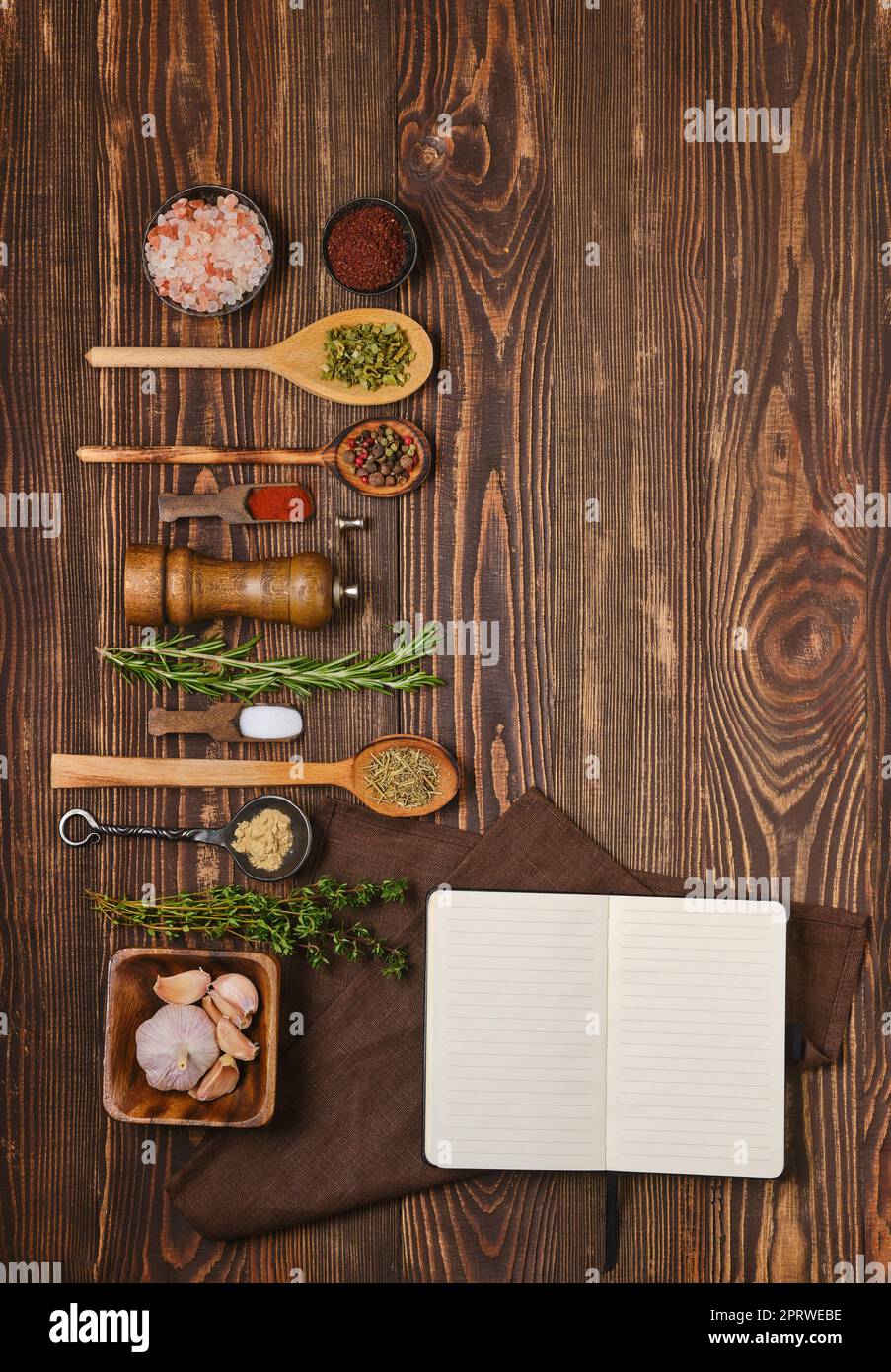 Overhead view of open cookbook for recipes laying next to kitchen spoons and bowls with spices and seasonings Stock Photo