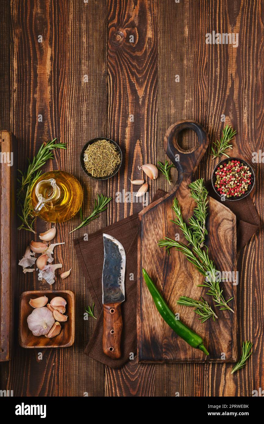 Top view of wooden cutting board with fresh rosemary and spices for piquant sauce or marinade Stock Photo