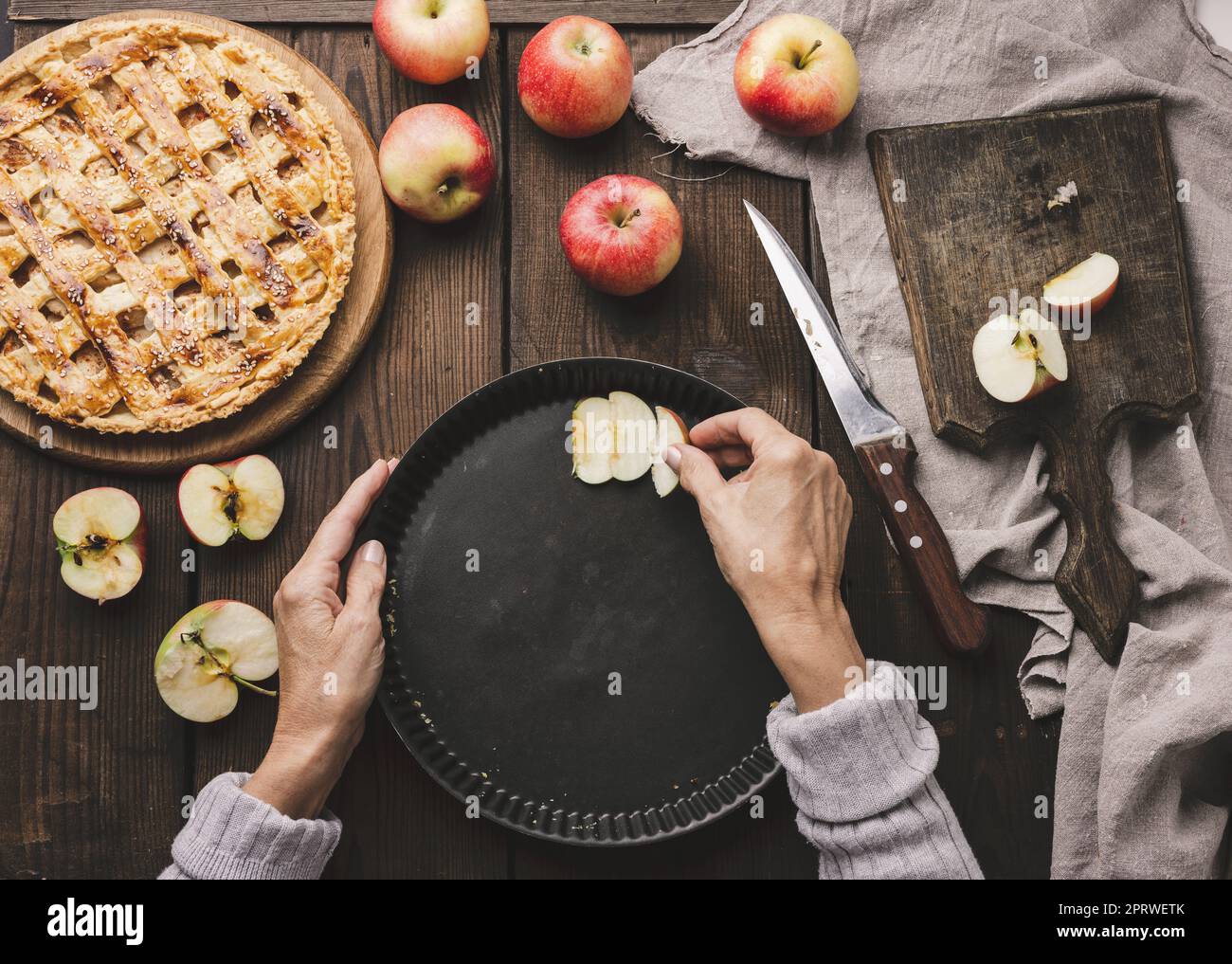 A woman puts apple slices in a round baking sheet on the table, next to the ingredients Stock Photo