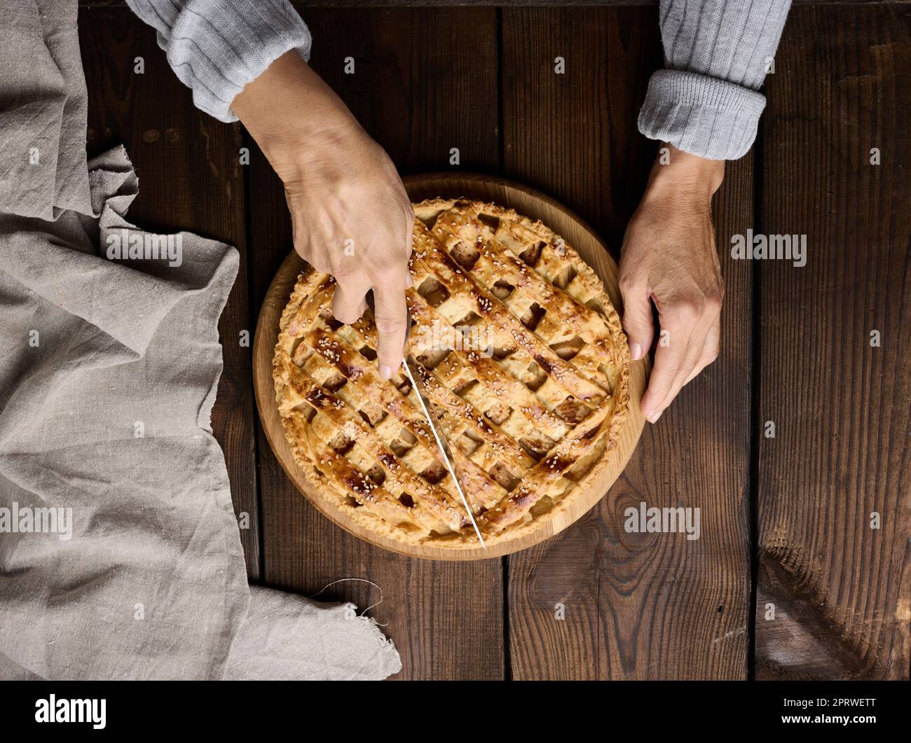 A woman cuts a baked round pie with apples with a knife on a wooden table Stock Photo