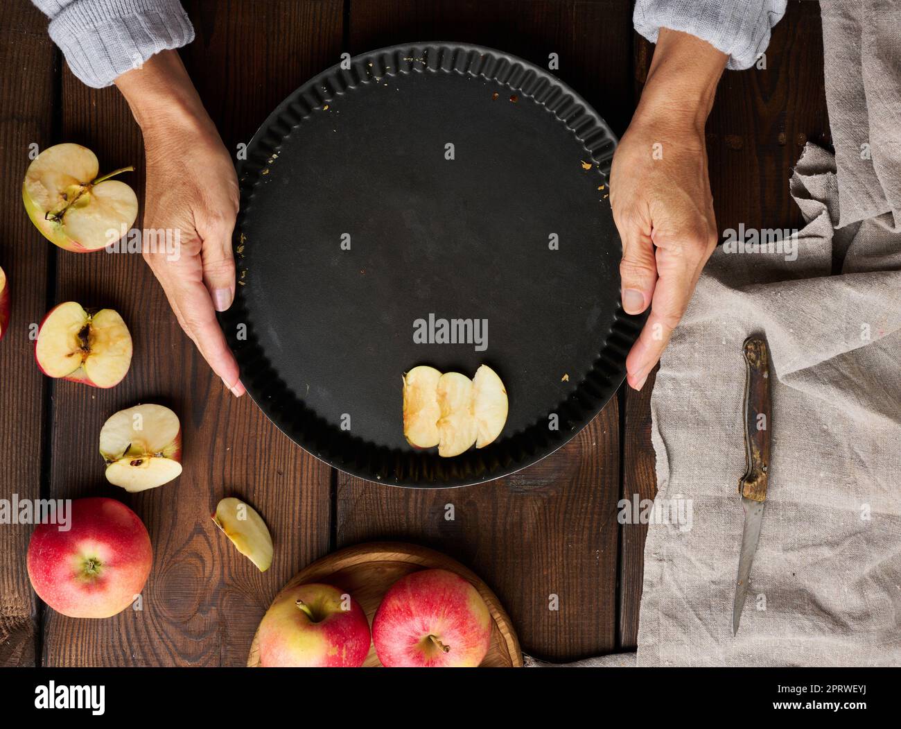 A woman puts apple slices in a round baking sheet on the table, next to the ingredients. View from above Stock Photo