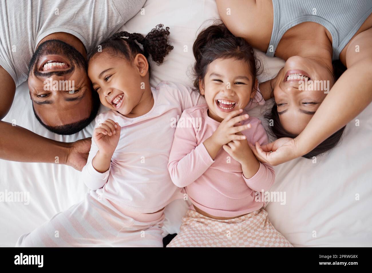 Happy family, love and morning tickling with parents and children lying and playing in bedroom for fun together at home from above. Laughing and man and woman spending time with playful kids to bond Stock Photo