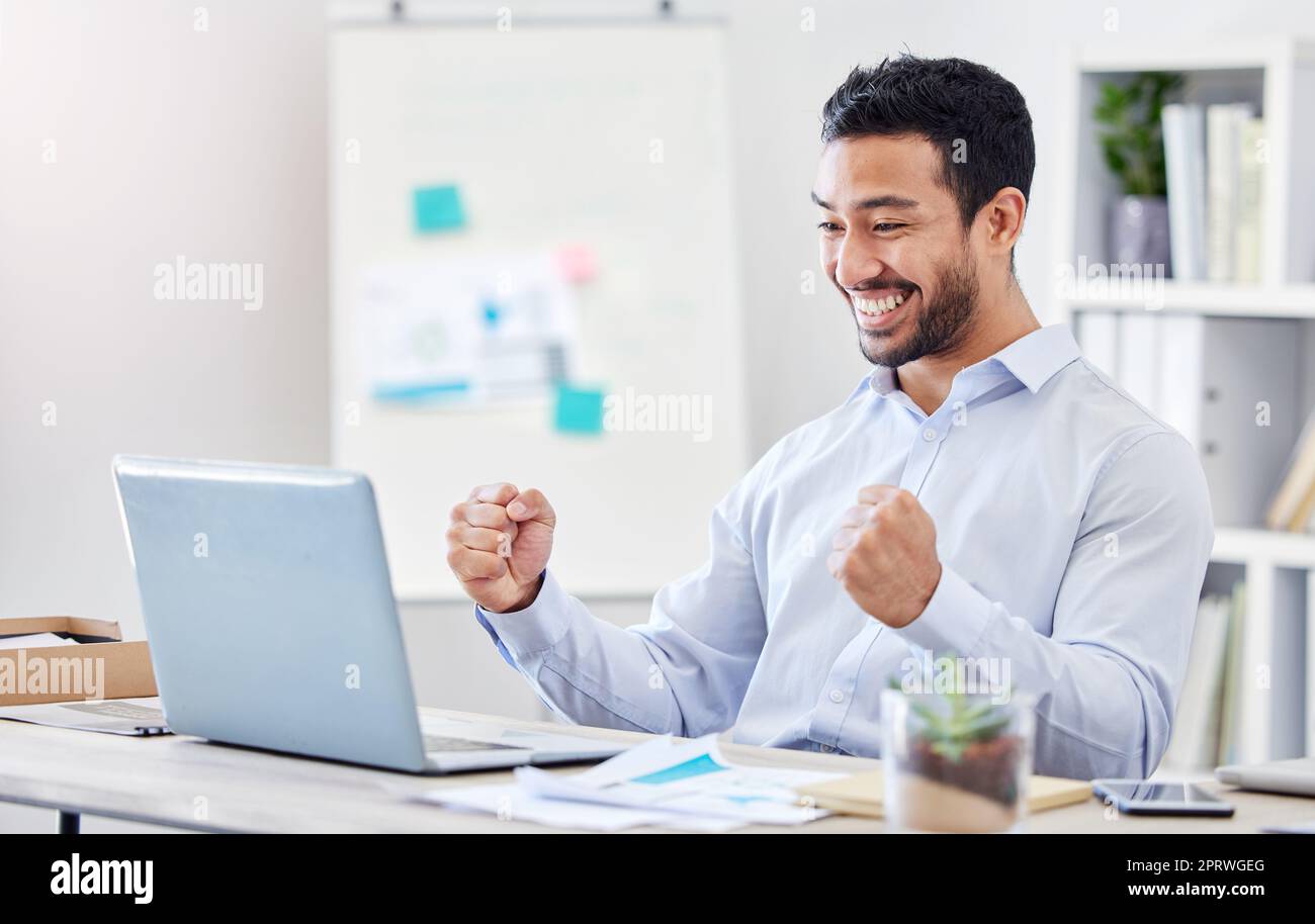 Motivation, success and yes with a business man in celebration and working on a laptop by his desk in the office. Email, good news and smile with a young and happy male employee cheering at work Stock Photo