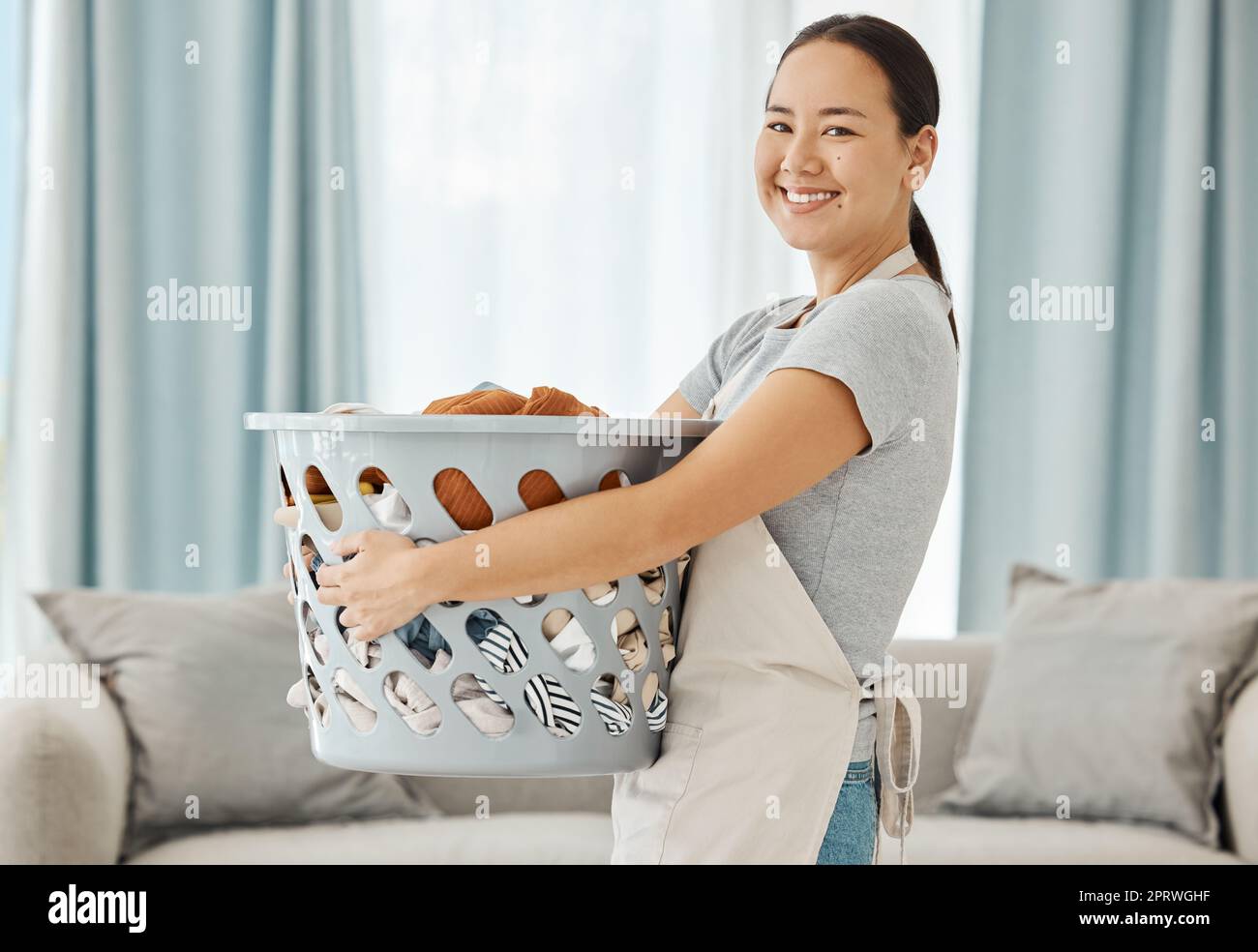 Happy Asian cleaner woman with laundry working for home, house or hotel hospitality cleaning help service agency. Japanese girl maid or worker smile in apartment with dirty clothes in washing basket Stock Photo