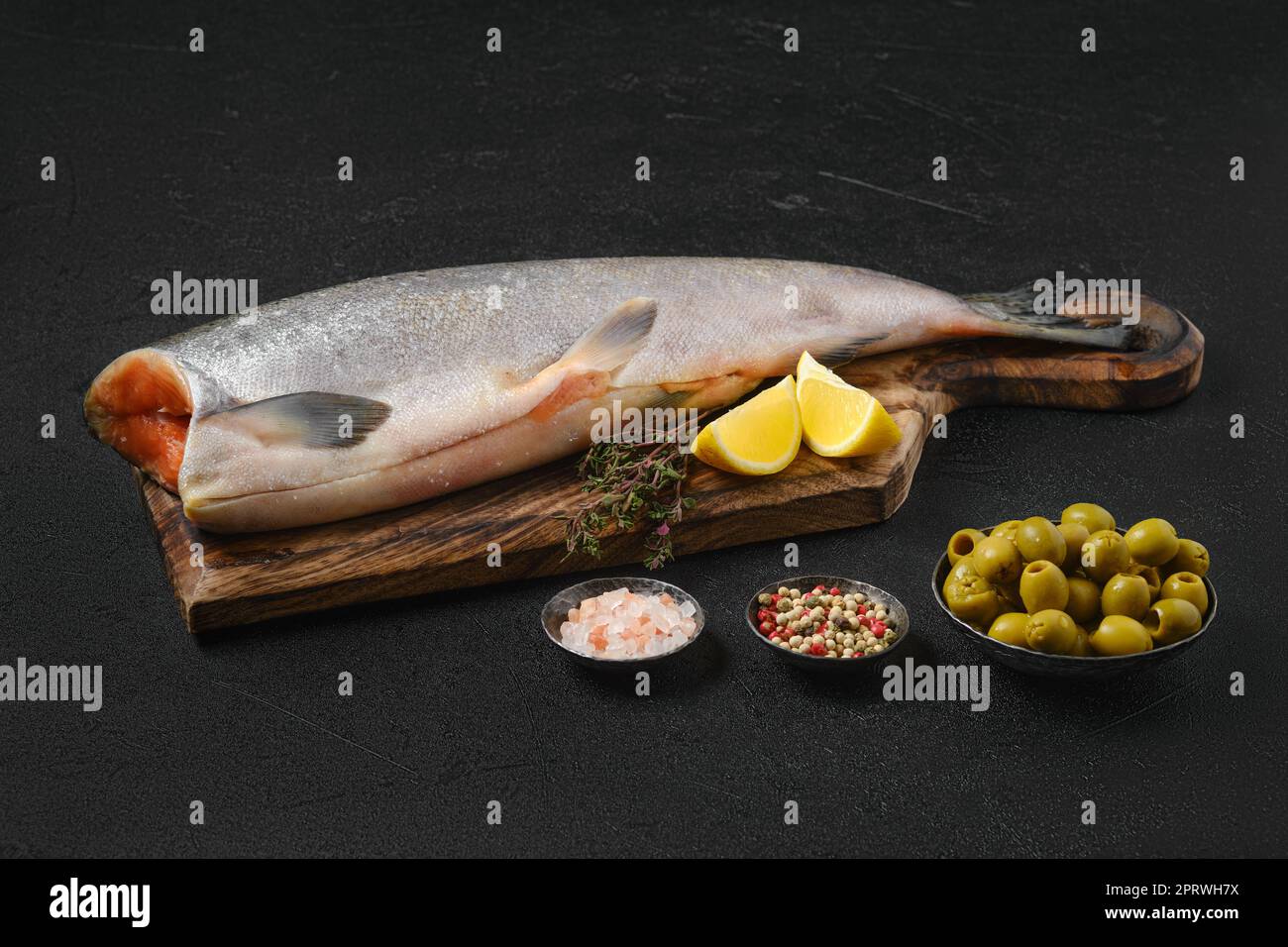 Headless chinook on wooden cutting board with spice and lemon Stock Photo