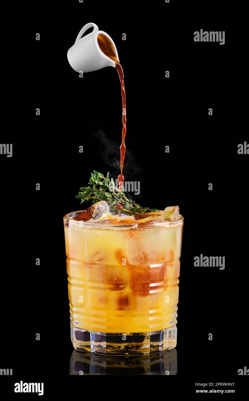 Pouring hot espresso in glass with tonic and orange syrup and thyme Stock Photo