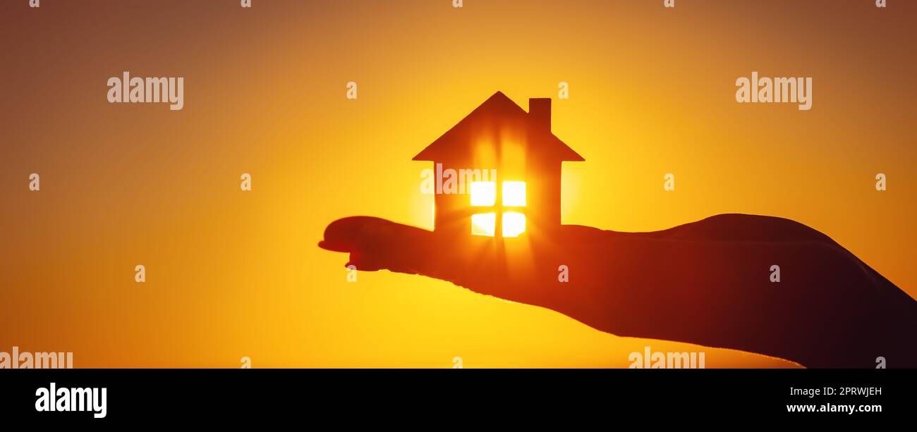 Woman's hand holding a model of a house on sunset evening Stock Photo