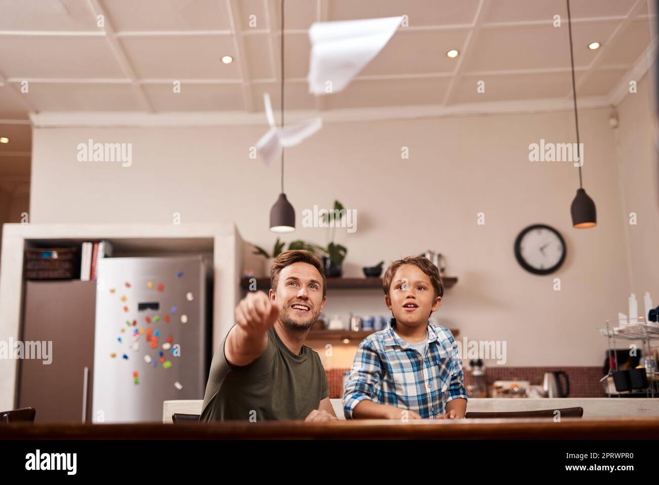 I want to be a pilot someday. a man and his young son playing with paper planes at home. Stock Photo