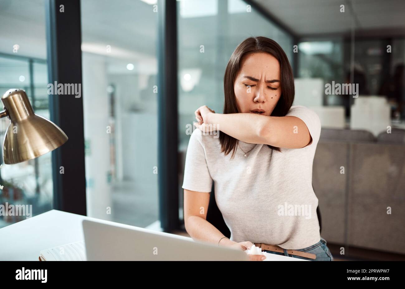 Practice good cough etiquette for the sake of everyones health. a young businesswoman coughing into her elbow in an office. Stock Photo