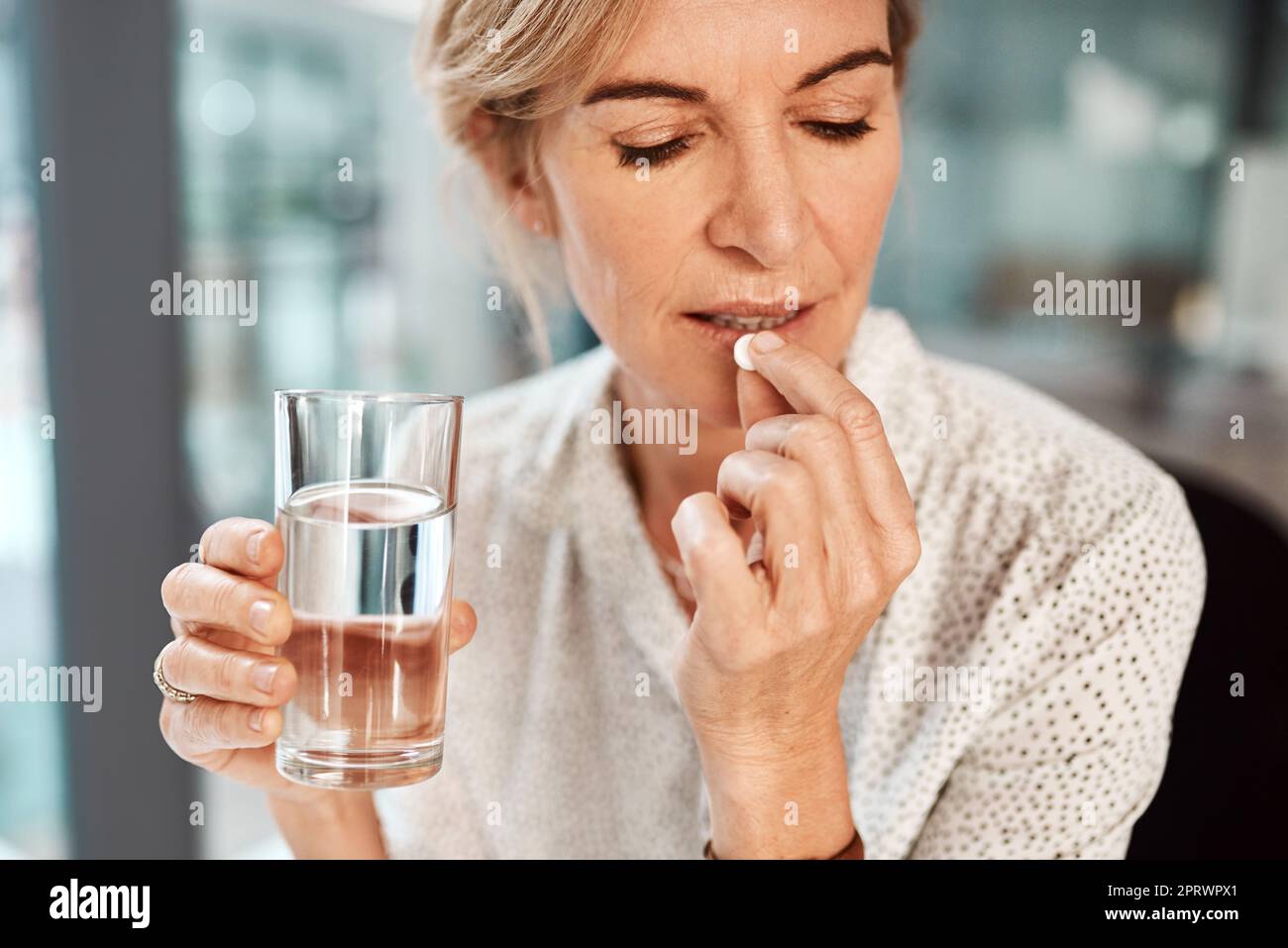 This aspirin should take care of my headache. a mature businesswoman taking medication in an office. Stock Photo