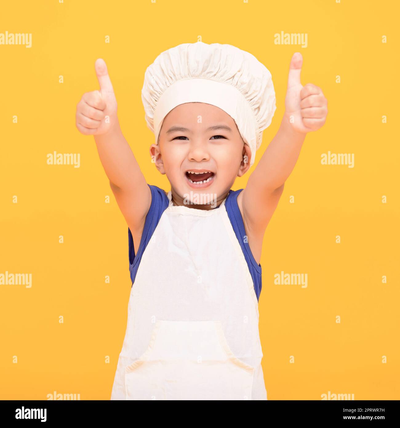 Happy boy in chef uniform showing thumbs up on yellow background Stock Photo