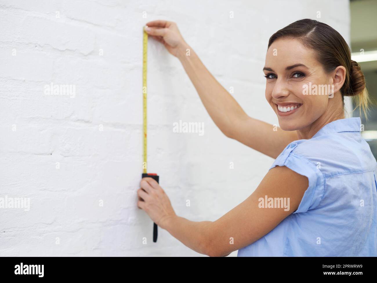 Perfect spot for my new painting. a smiling woman making measurements on a wall. Stock Photo
