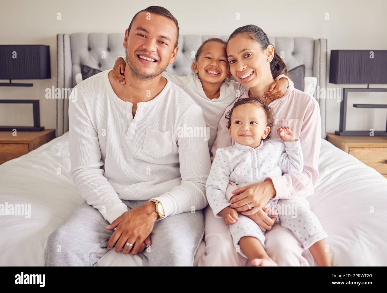 Family happy, portrait smile and relax on bed together in home, parents love for children in the morning and happiness in bedroom. Mother and father relaxing with kids and caring on the weekend Stock Photo