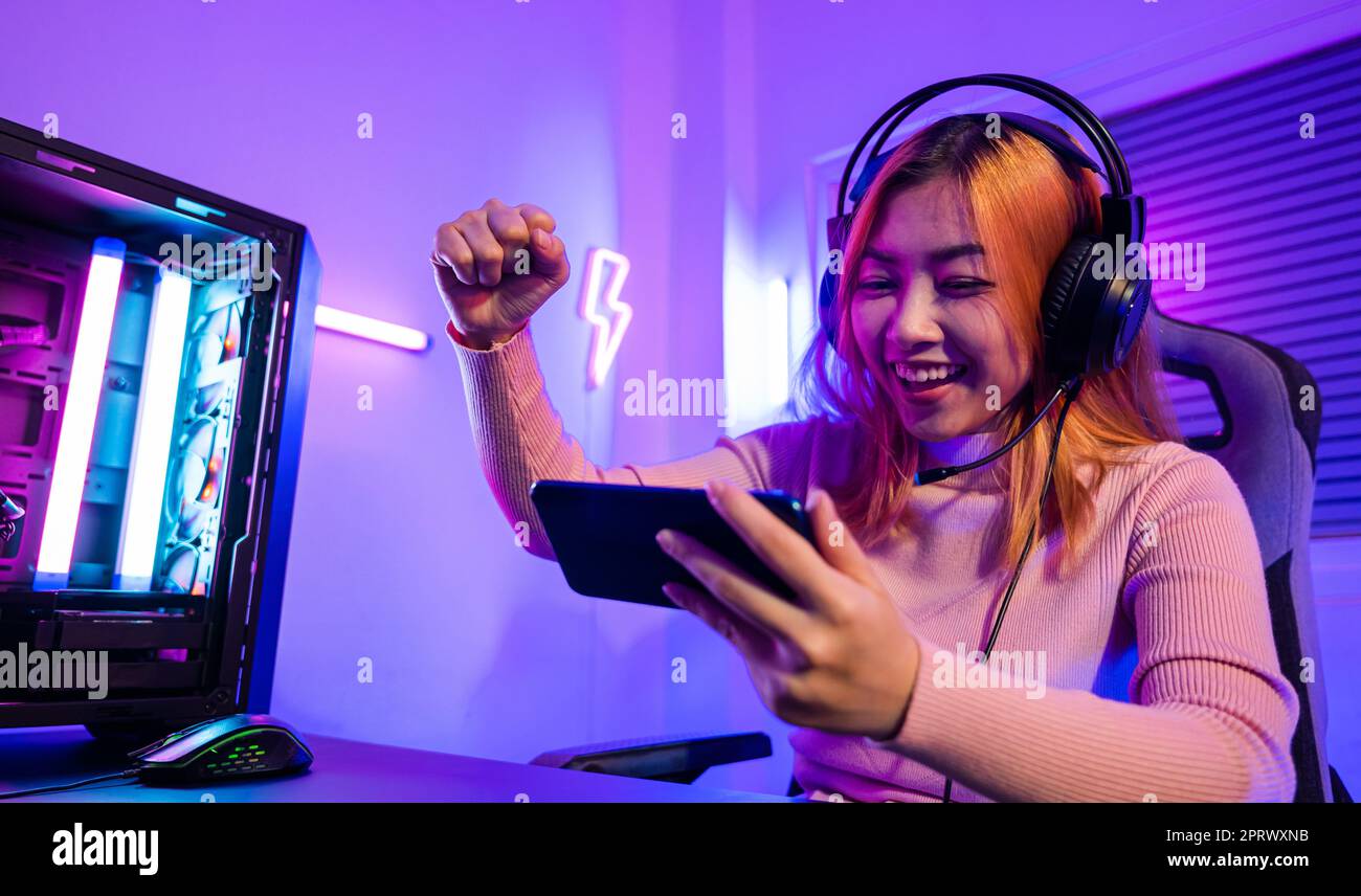 Happy Asia Girl Gamer Wear Headphone Competition Play Video Game Online  With Smartphone Colorful Neon Lights In Living Room At Home. Esport  Streaming Game Online, Home Quarantine Activity Concept. Stock Photo,  Picture