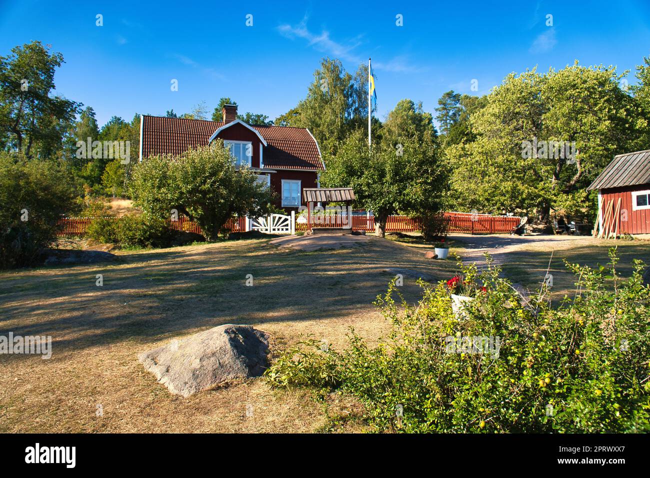 Swedish red and white traditional house in Smalland, White fence green garden blue sky Stock Photo