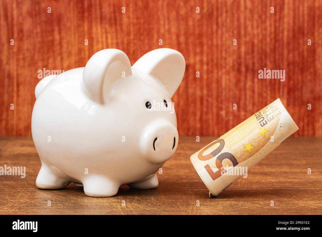 Piggy bank looking at falling roll of fifty euros Stock Photo