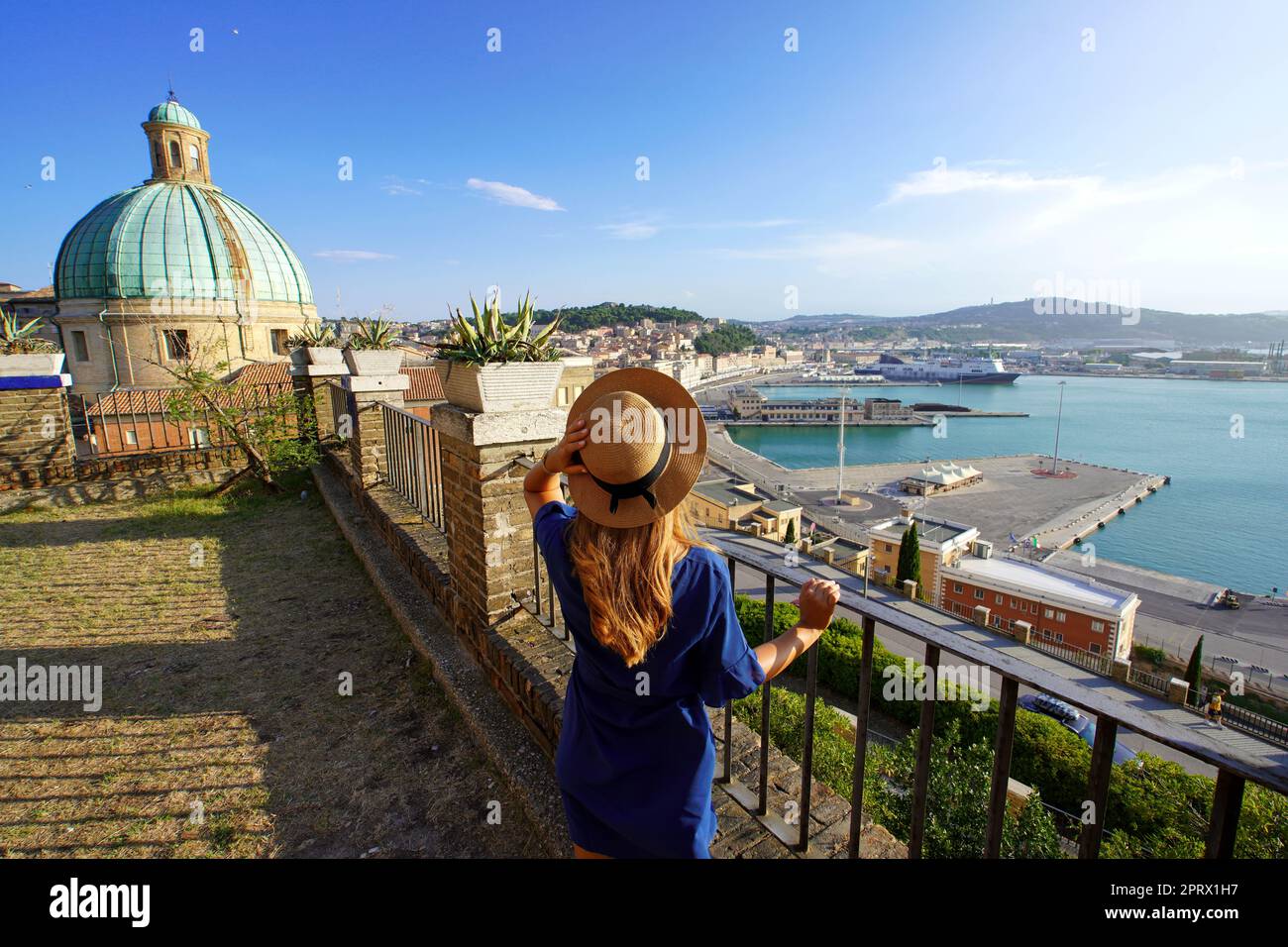 Tourism in Ancona, Italy. Back view of traveler woman enjoying view of Ancona city and seaport from terrace, Marche, Italy. Stock Photo