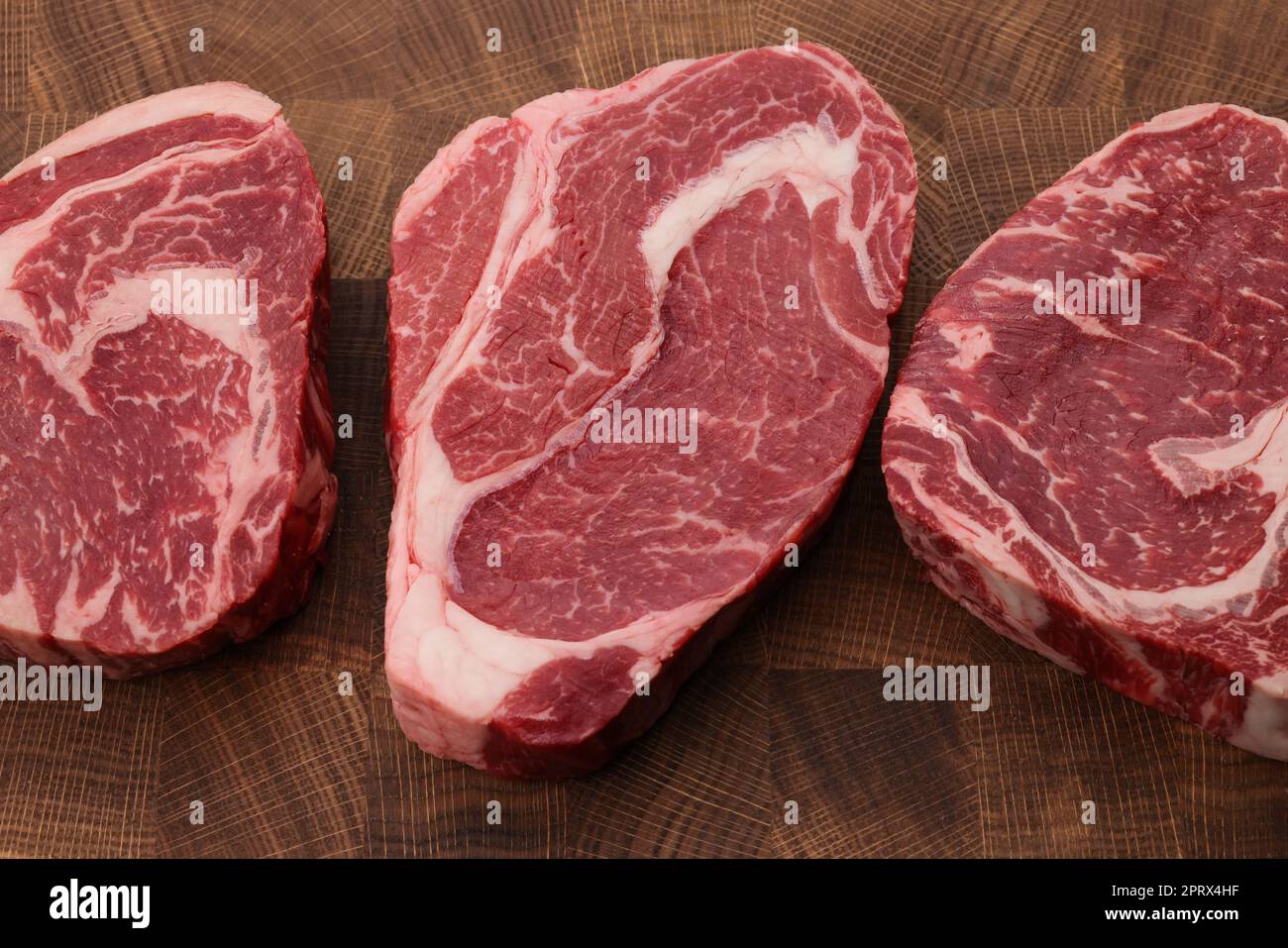 Three raw ribeye beef steaks on cutting board Stock Photo