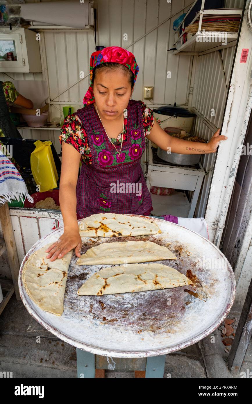 A young indigenous Zapotec woman makes yellow mole empanadas on a comal griddle in Tlacolula de Matamoros, Oaxaca, Mexico. Stock Photo