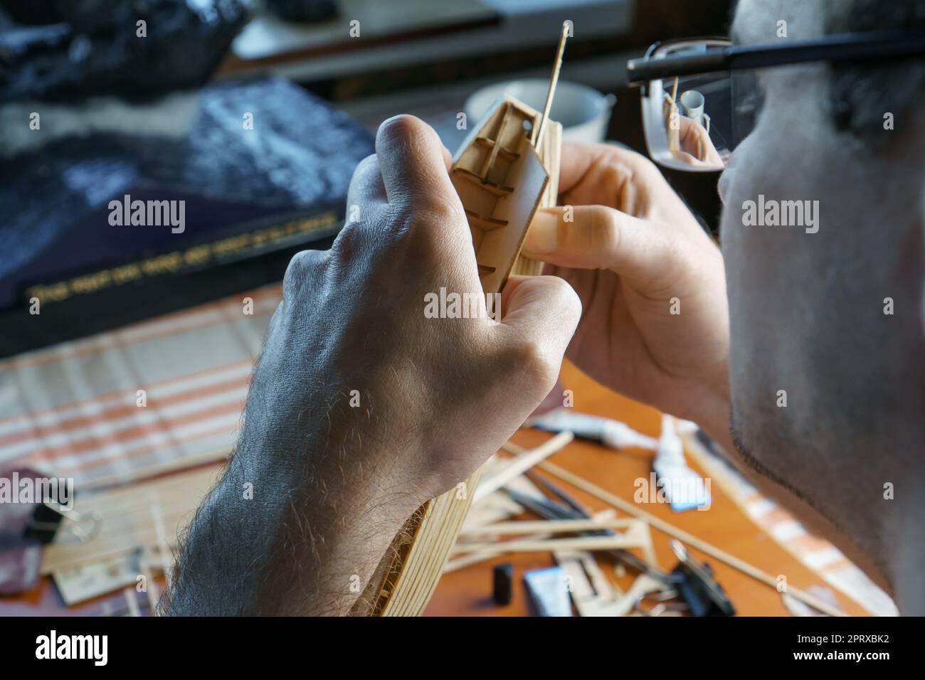 Hands of man gluing plywood details for ship model with glue, holding with fingers. Process of