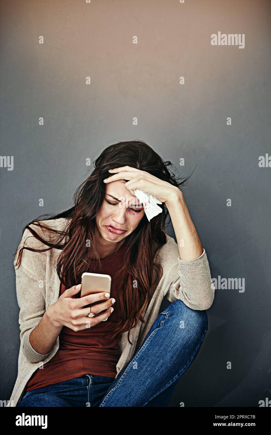 It happens everytime. a beaten and bruised young woman crying while looking at her cellphone Stock Photo