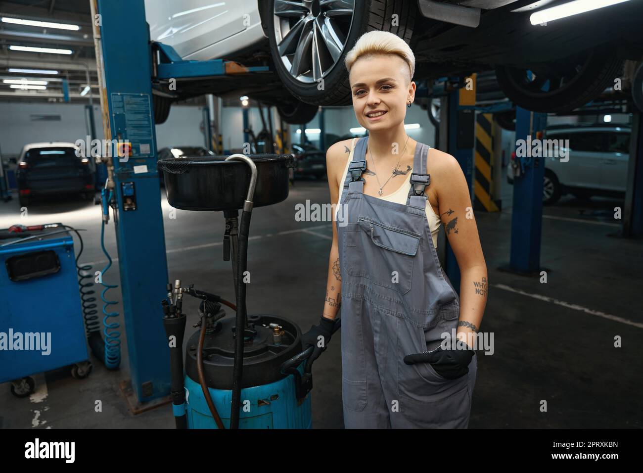 Pretty car mechanic stands with a device for draining oil Stock Photo