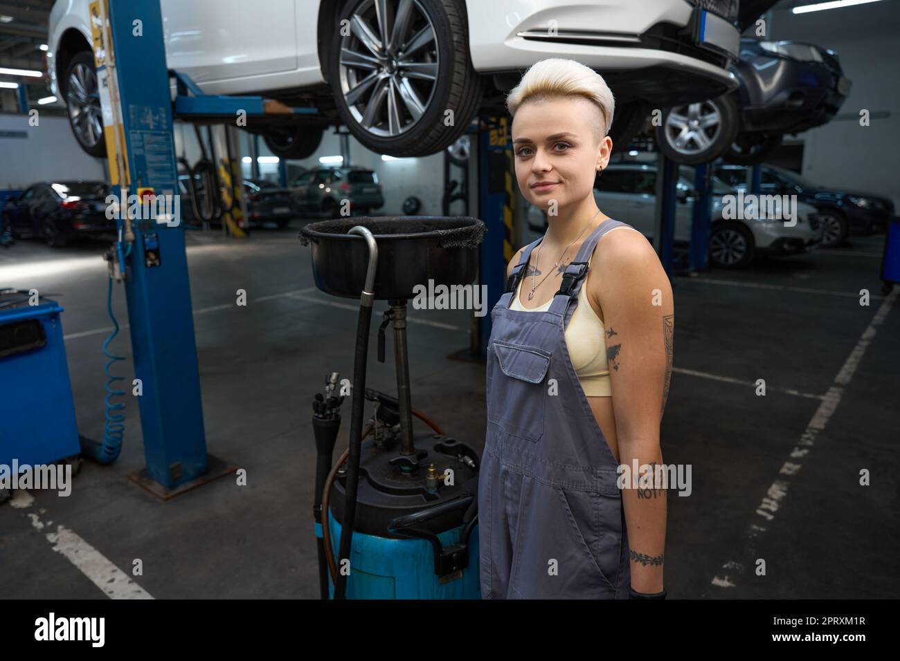 Woman auto repairman stands with a device for draining oil Stock Photo