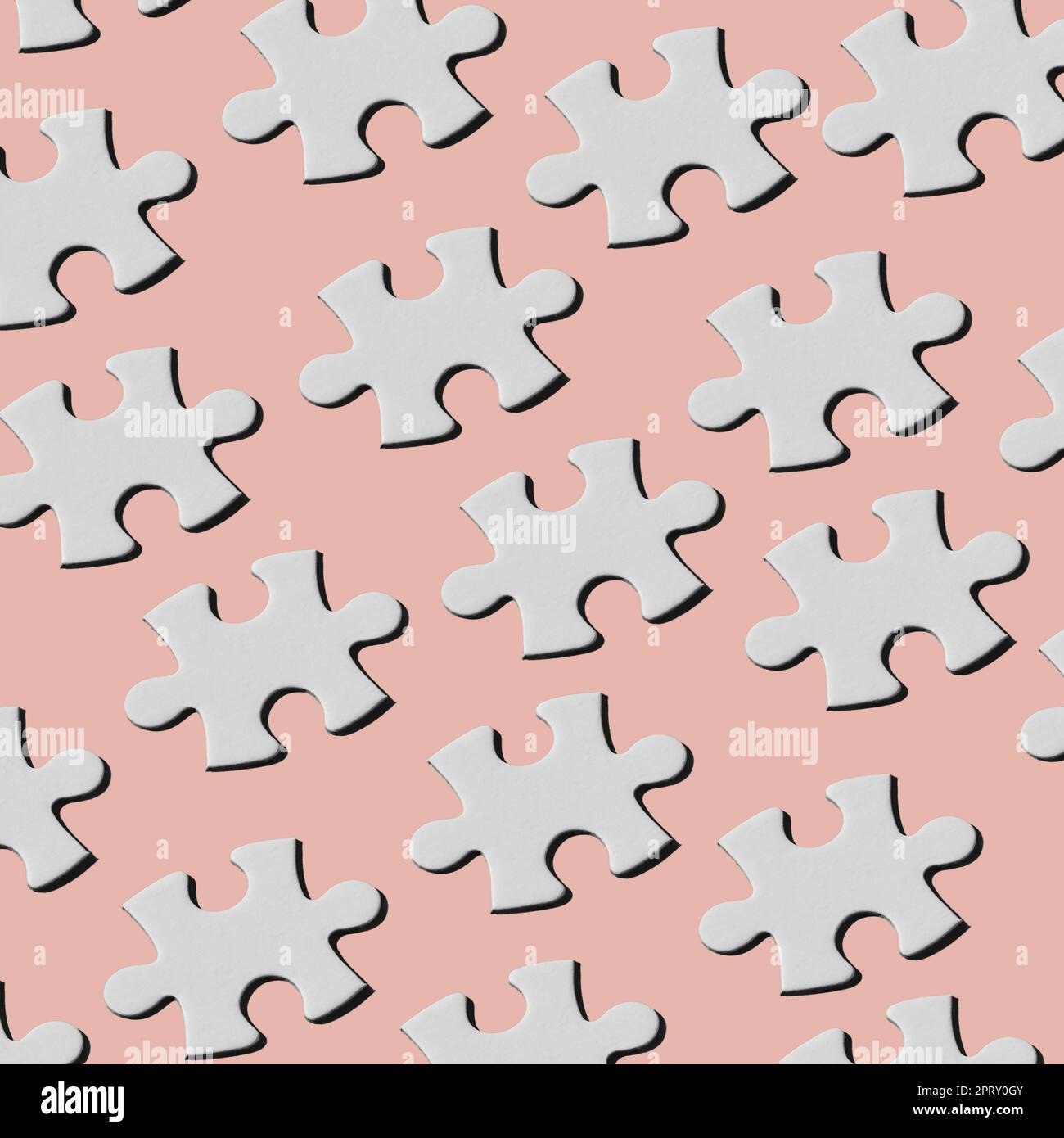 a pattern of white puzzle pieces arranged in different lines on a pale pink background Stock Photo