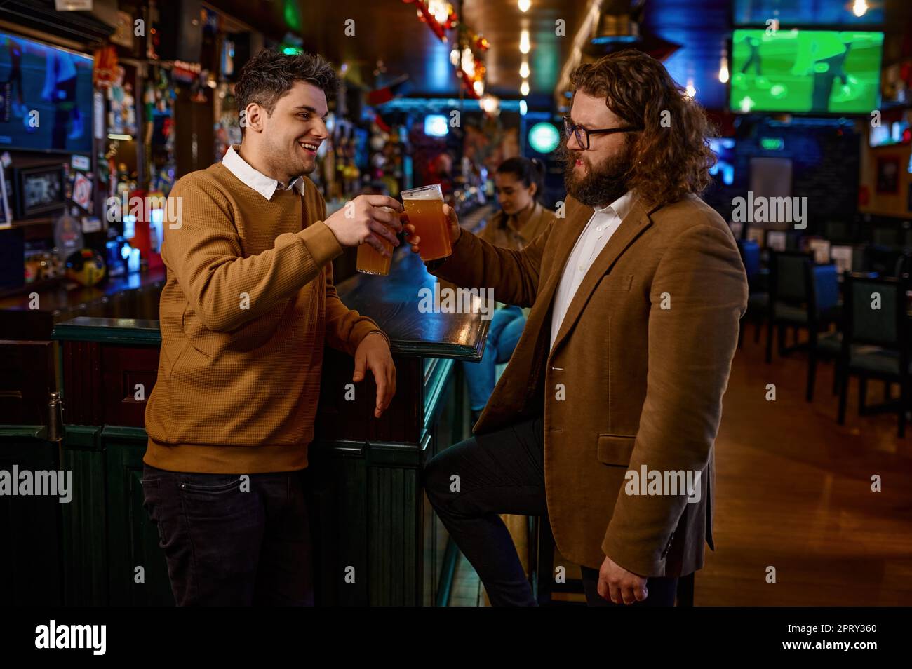 Happy male friends clinking with beer mugs in pub. Young people having fun together. Friendship concept Stock Photo