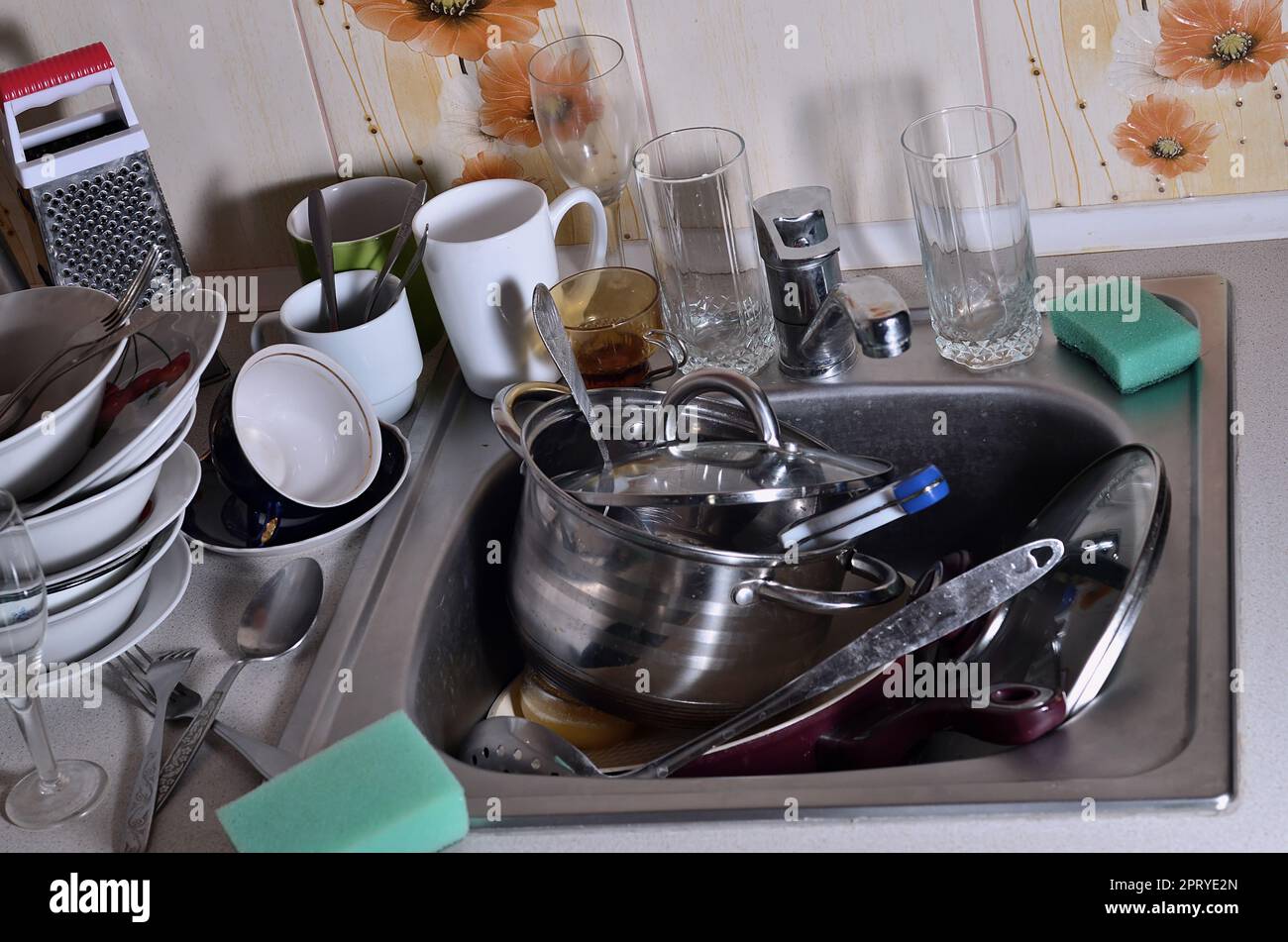 A huge pile of unwashed dishes in the kitchen sink and on the countertop. A lot of utensils and kitchen appliances before washing. The concept of dail Stock Photo