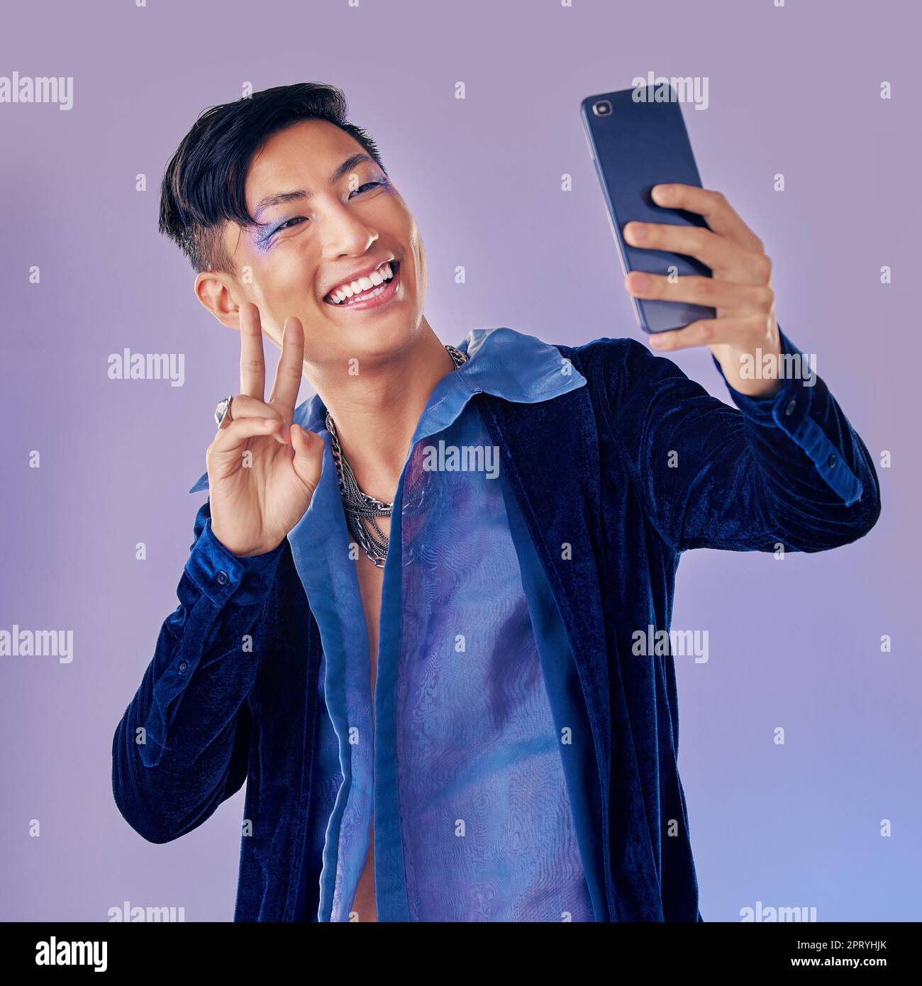 Man, makeup art and selfie with phone for creative, skin or beauty with happiness against purple backdrop. Happy, model and photo with smartphone with Stock Photo