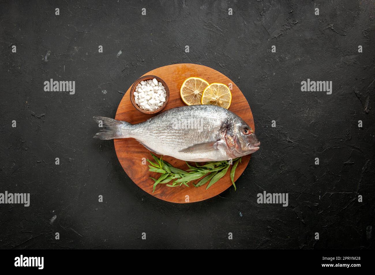 top view tarragon raw sea fish sea salt in bowl on round wood board on ...