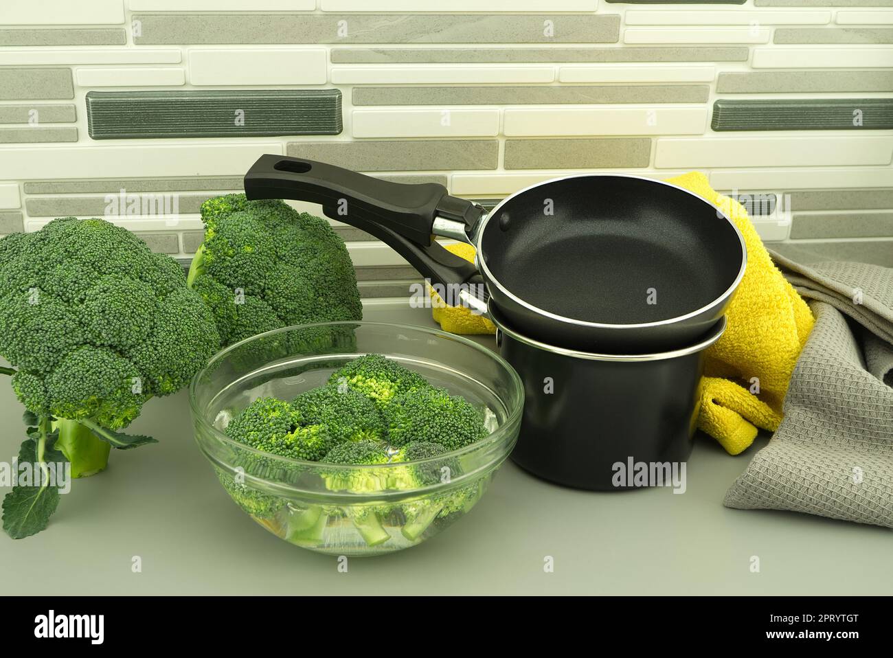 Fresh broccoli florets soaked in a clear bowl of water next to the pan ...