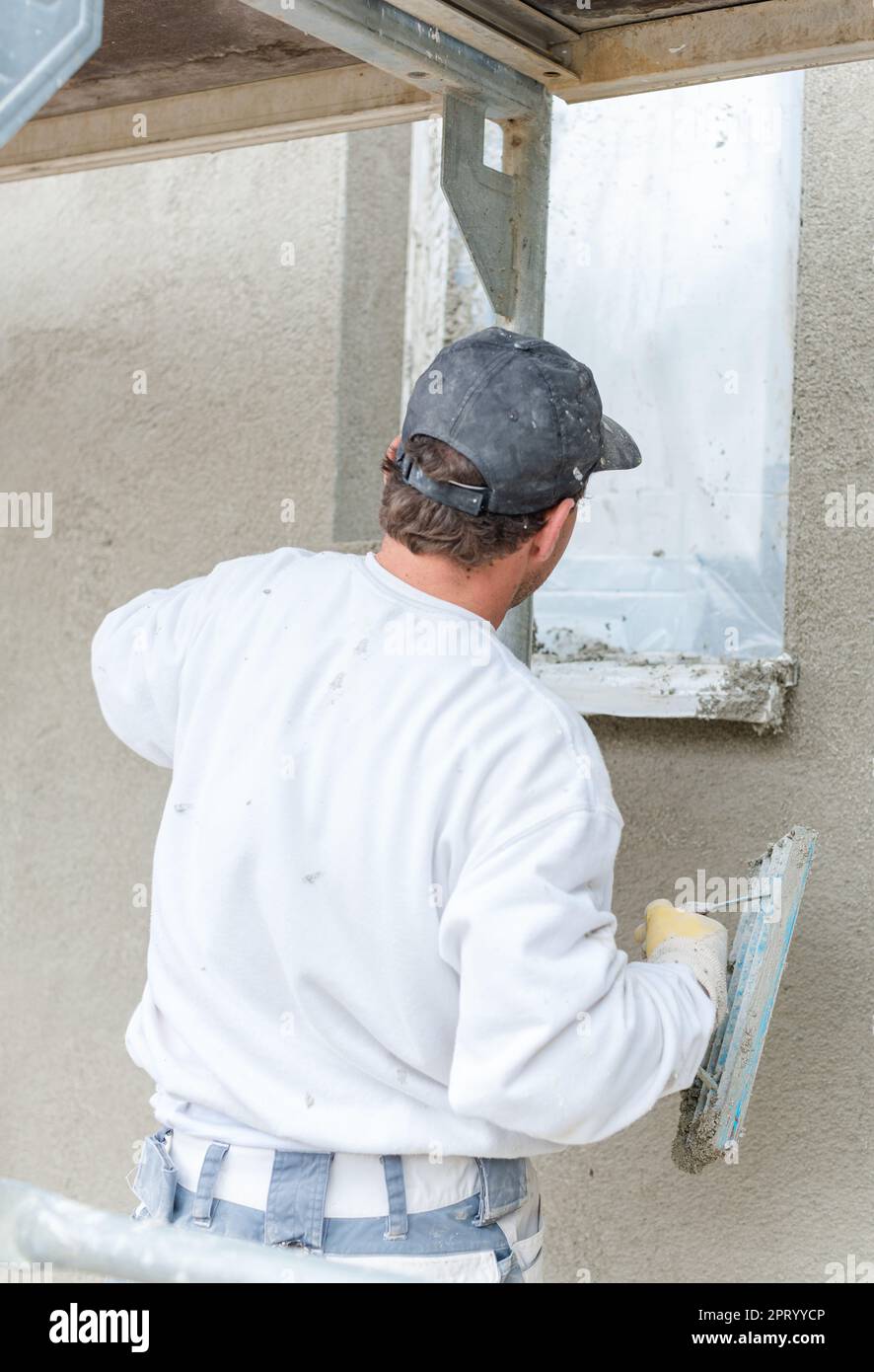Plasterer smoothing plaster on a facade standing on scaffold Stock Photo