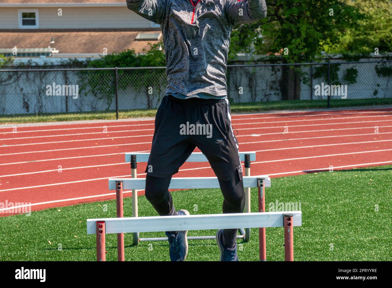 Front view of a high school boy jumping over hurdles while working out