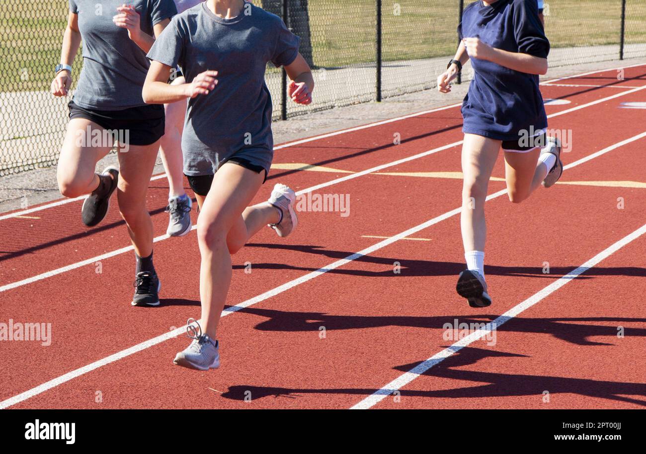 Front view of three high school girls running fast in lanes on a red