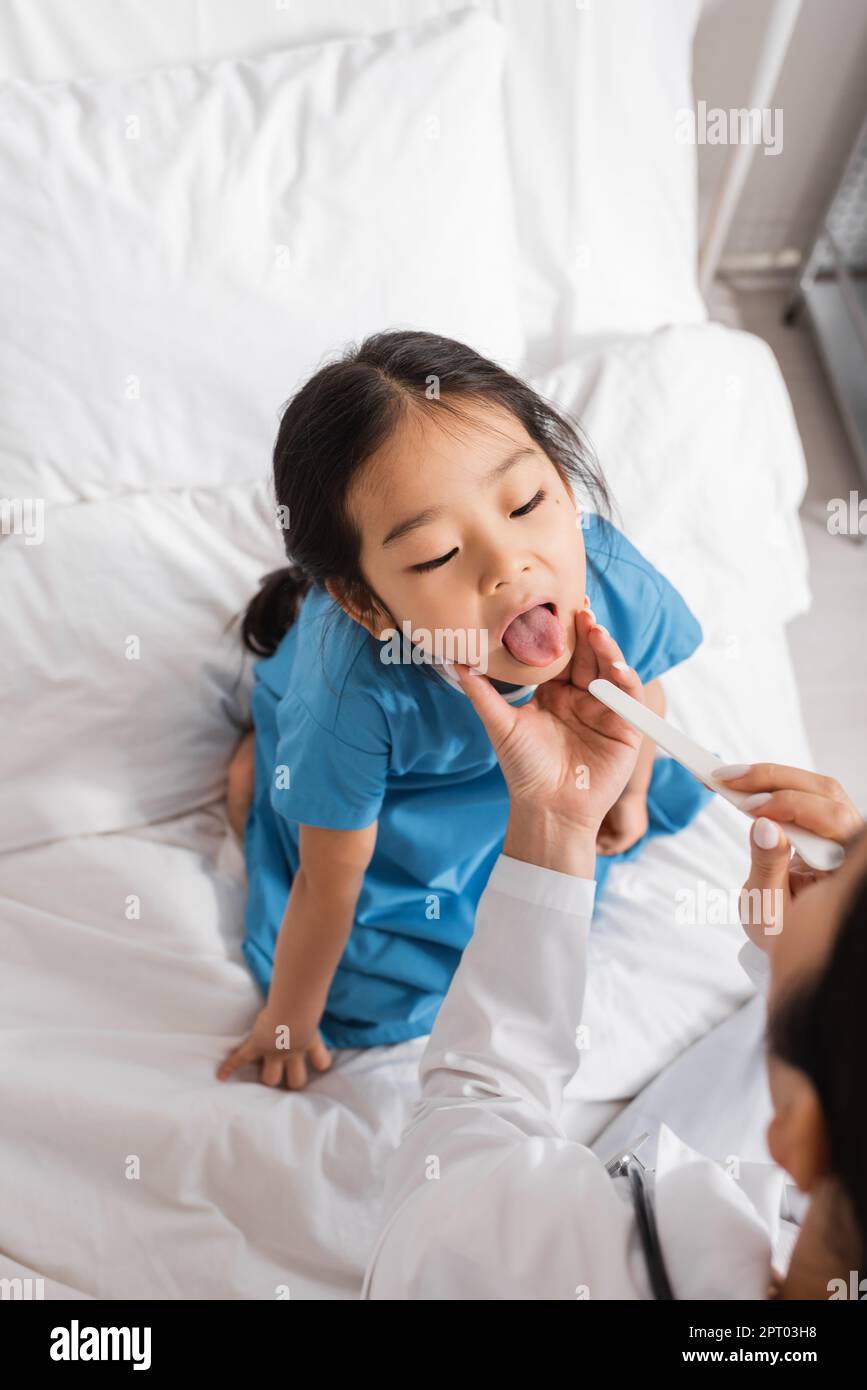 high angle view of asian girl opening mouth near doctor with tongue