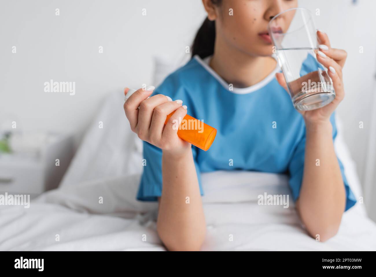 partial view of sick woman holding pills container and drinking water in hospital ward,stock image Stock Photo