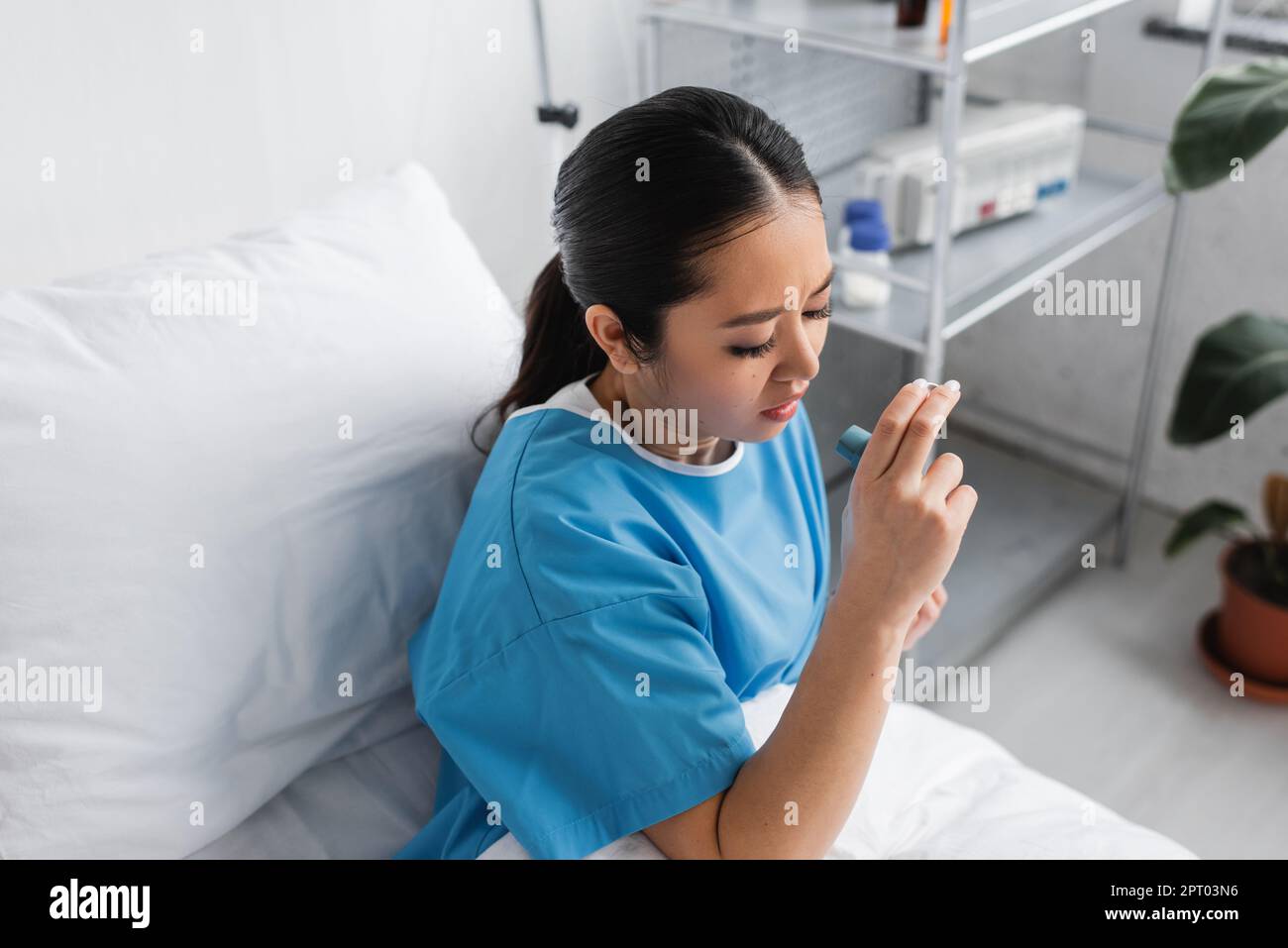 high angle view of sick asian woman holding inhaler while sitting on bed in hospital ward,stock image Stock Photo