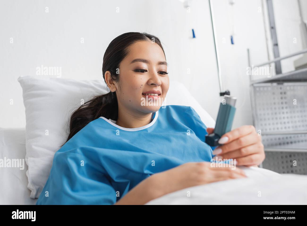 happy asian woman in hospital gown lying on bed in clinic and looking