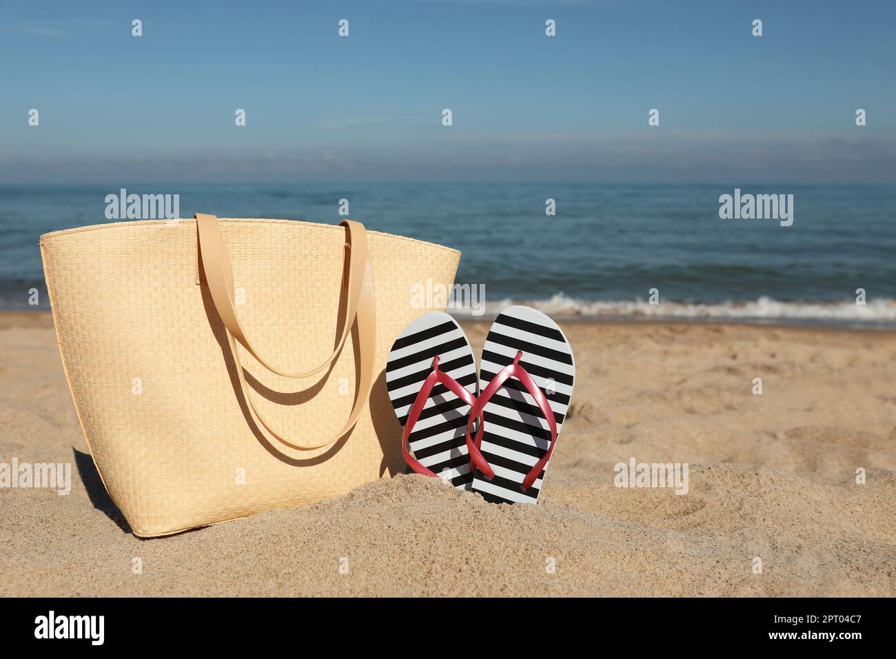 Striped flip flops and beach bag on sandy seashore, space for text ...