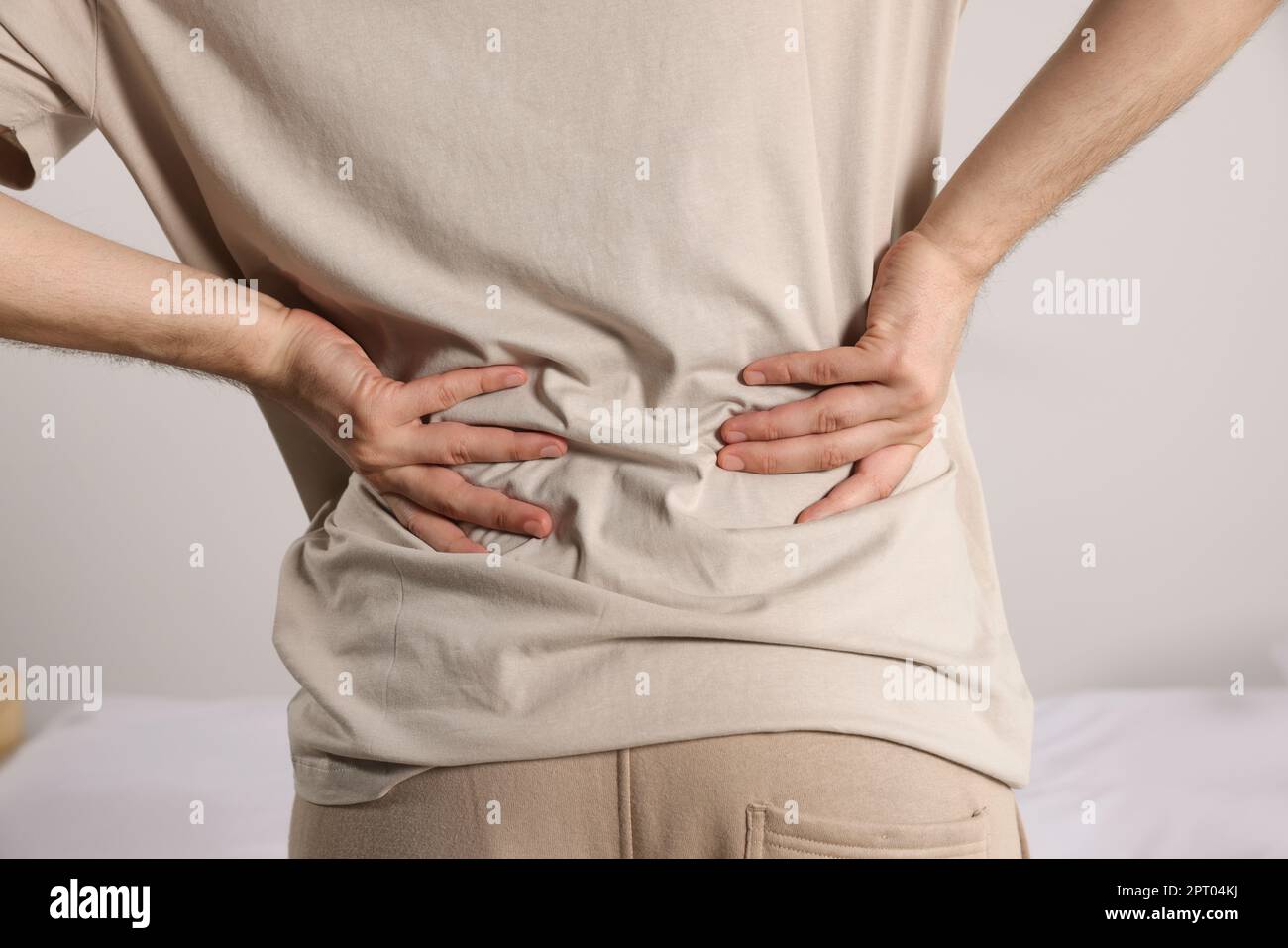 Man suffering from back pain while standing near bed in room, closeup. Symptom of scoliosis Stock Photo