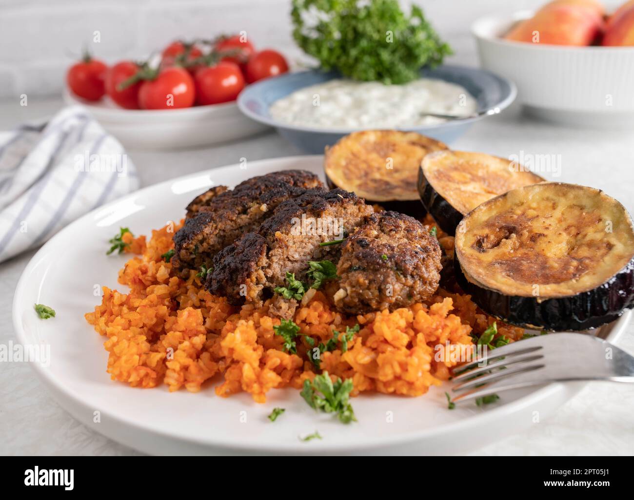 Greek bifteki with feta cheese, tomato rice and fried eggplant on a plate Stock Photo