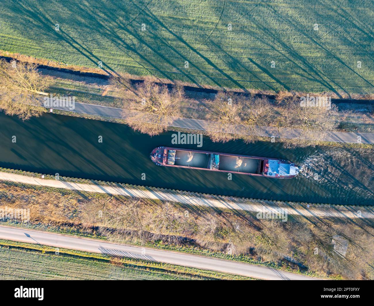 Aerial view from a drone of a cargo canal ship passes by over the canal on a sunny winter day, reflections are to be seen in the water, canal system in the outskirts of Rijkevorsel, Belgium. High quality photo Stock Photo