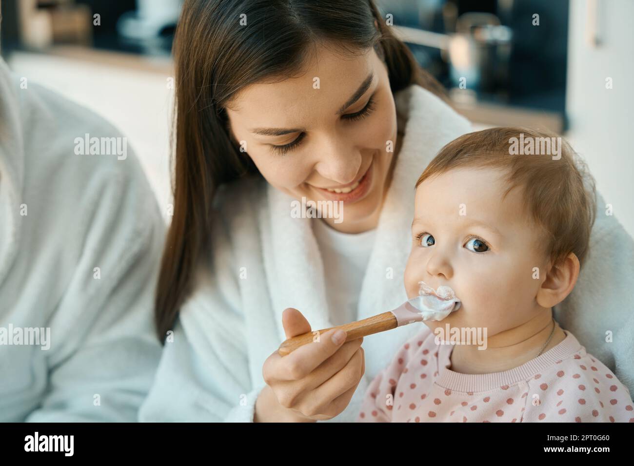 Happy female feeds the baby with a small spoon, the girl has plump cheeks Stock Photo