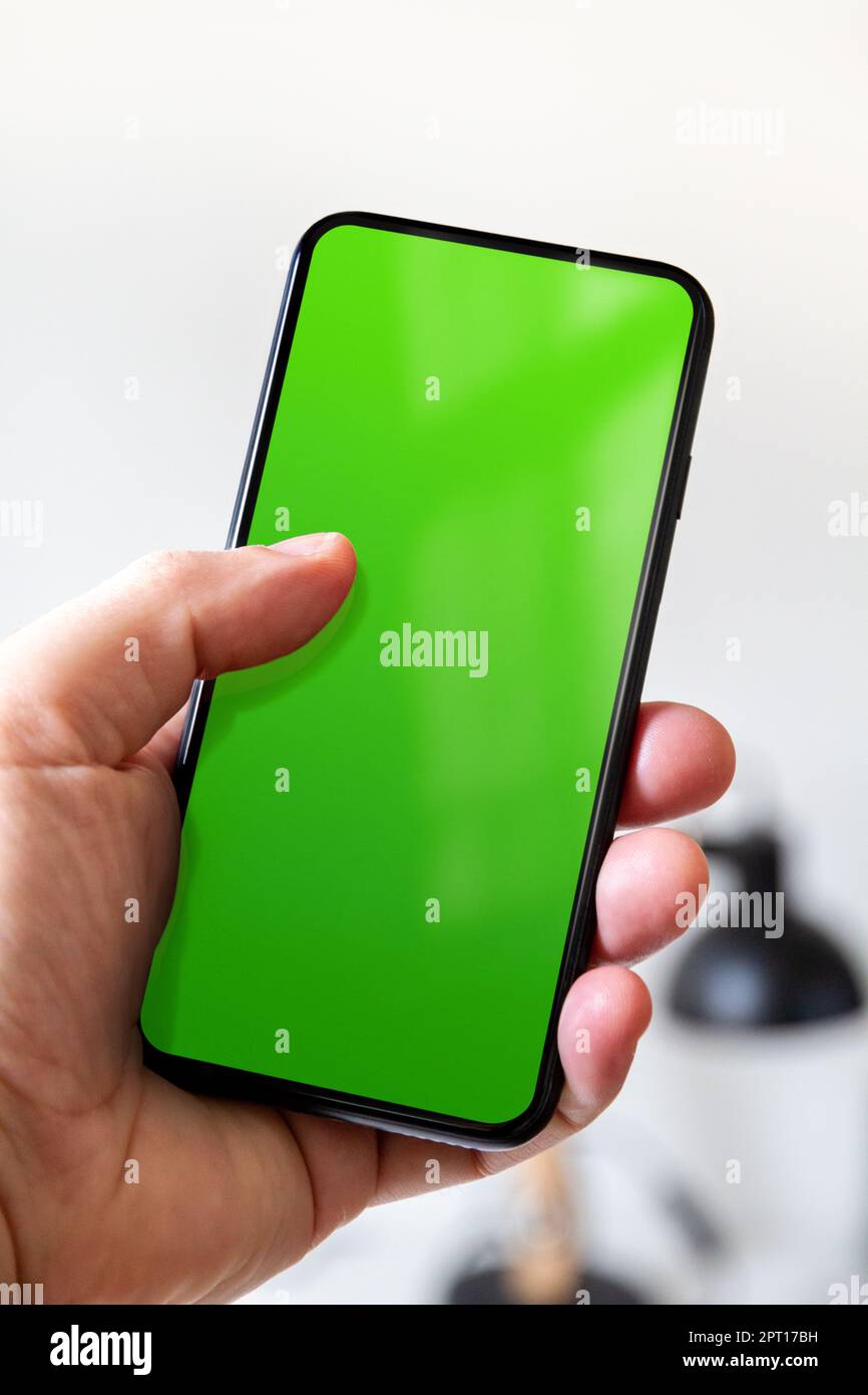 Hand holding a smartphone with blank green screen. White office