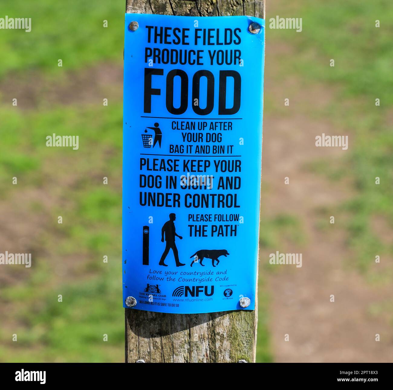 A sign on a wooden post saying 'these fields produce food - please control your dog' and 'clean up after your dog' 'bag it and bin it', England, UK Stock Photo